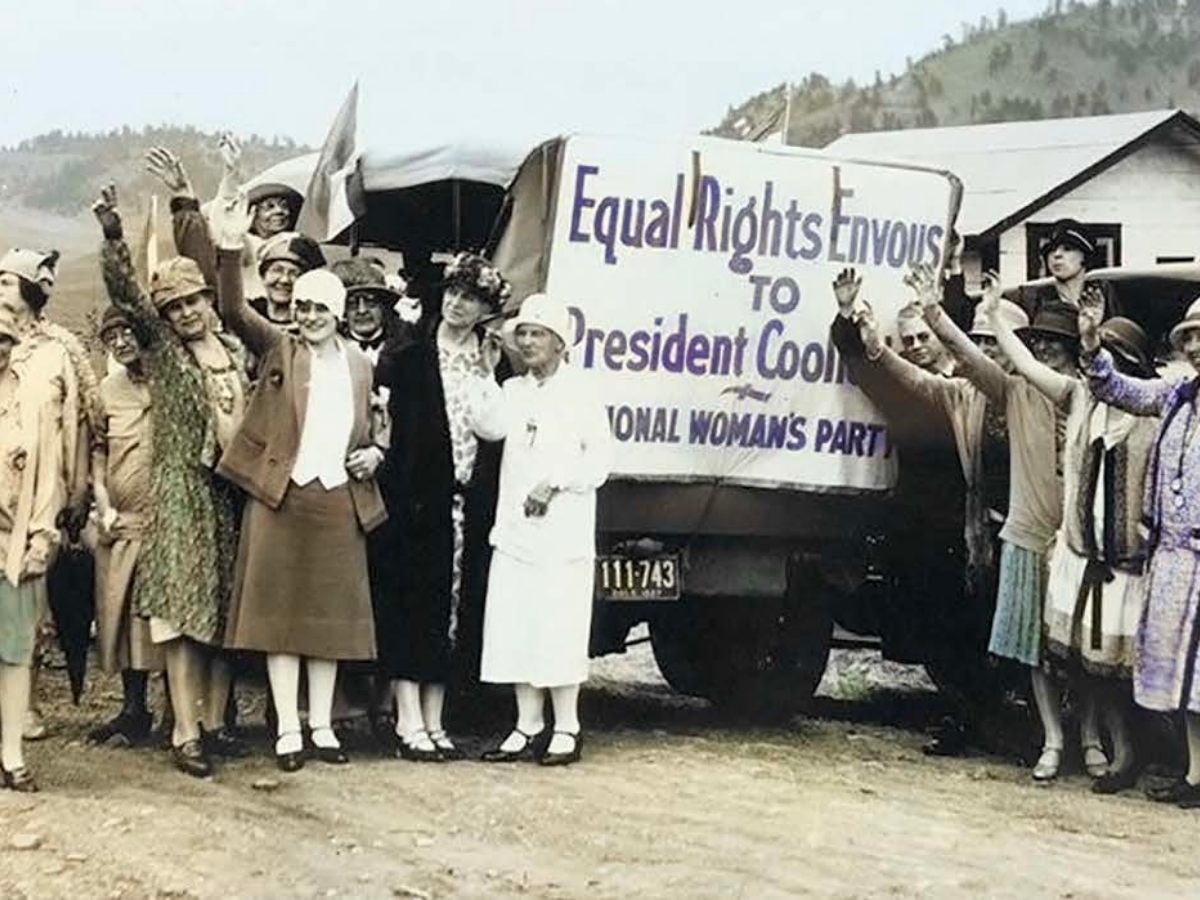A group of women standing in front of a sign that reads Equal Rights Envous to President Coolidge -- National Woman's Party
